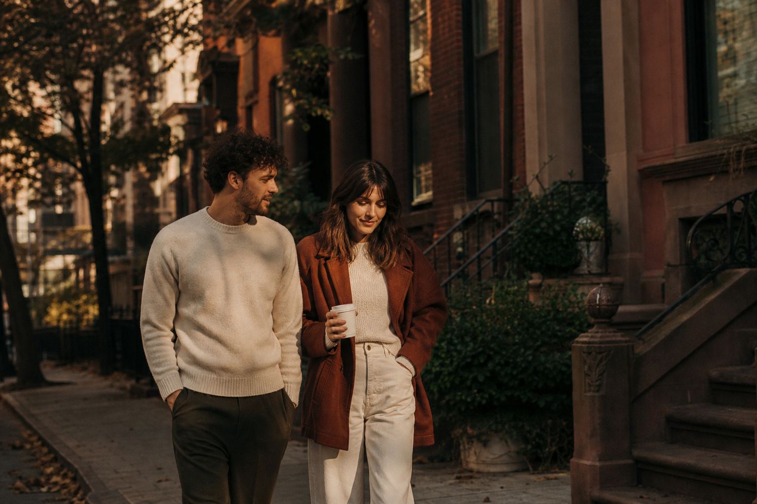 A couple walking down a brownstone street at golden hour